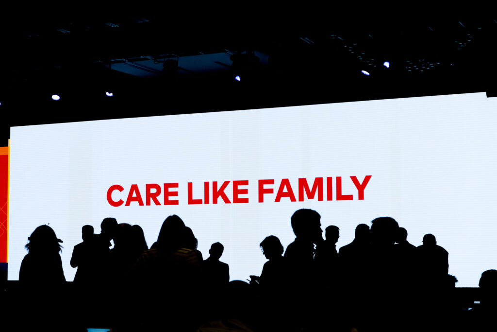 Event Photography of Employees mingling silhouetted against a screen that reads "care like family" in the background