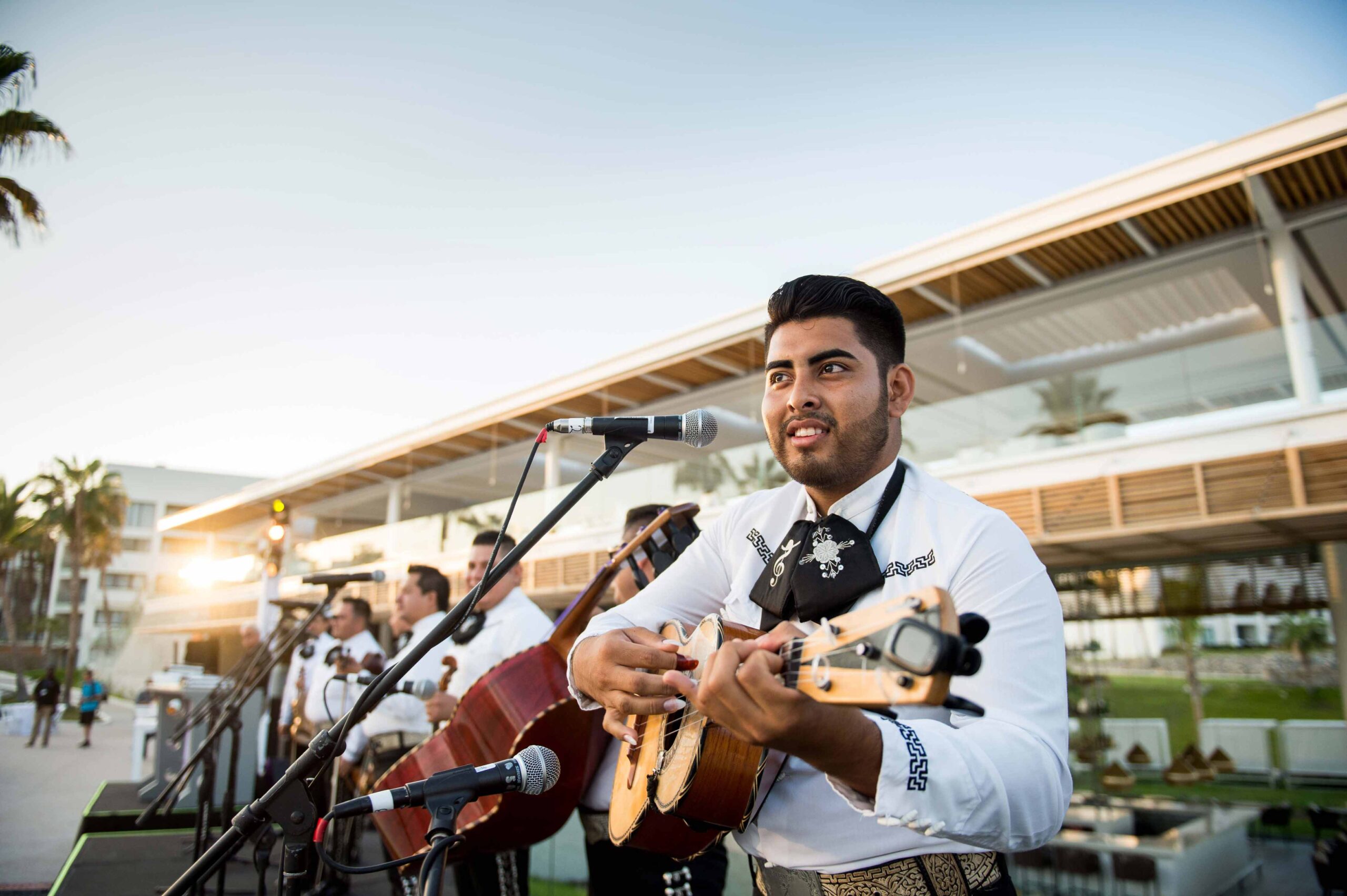 Mariachis perform outside a resort at at a welcome reception for a corporate celebration. Featured mariachi is singing and strumming the guitar. 