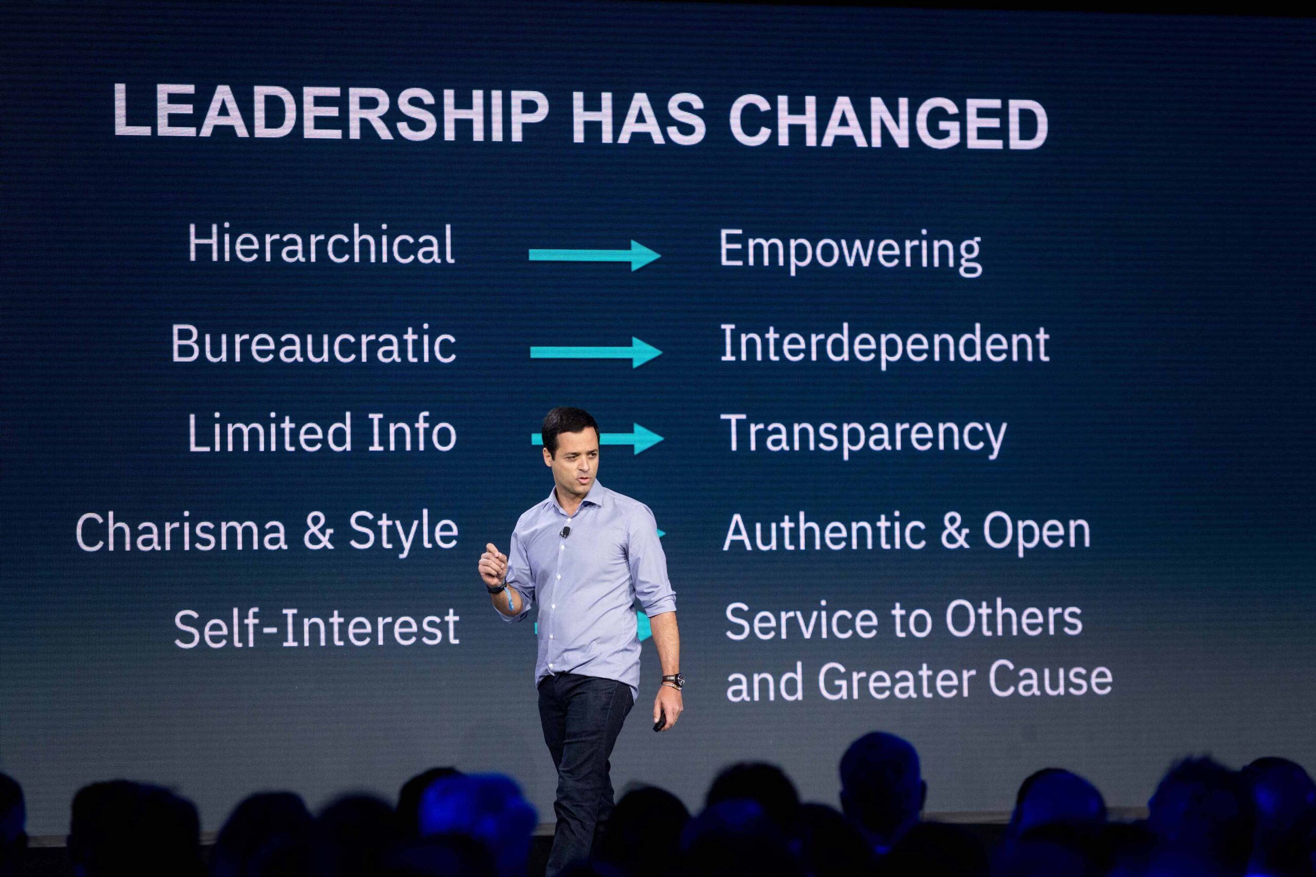 "Leadership has changed" is displayed in the background as a speaker walks the stage with attendees in the front row. The event photographer is using composition effectively.