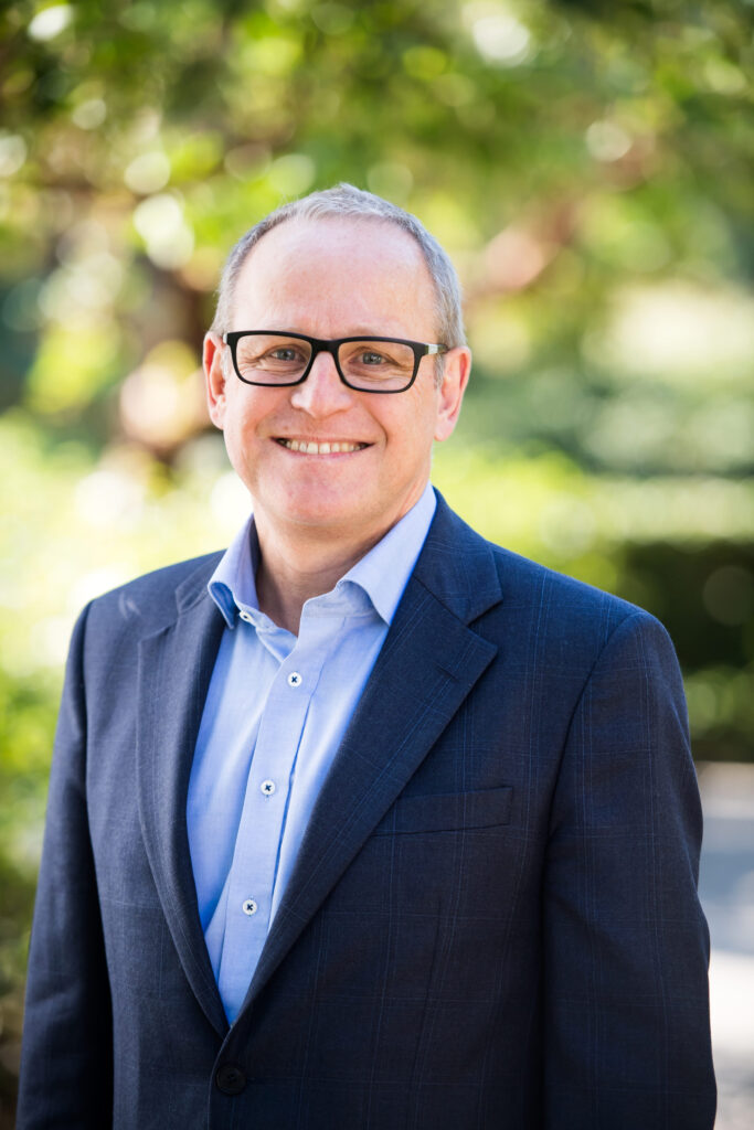 Man wearing a blue formal shirt and dark blue suit jacket happily posing for a professional headshot