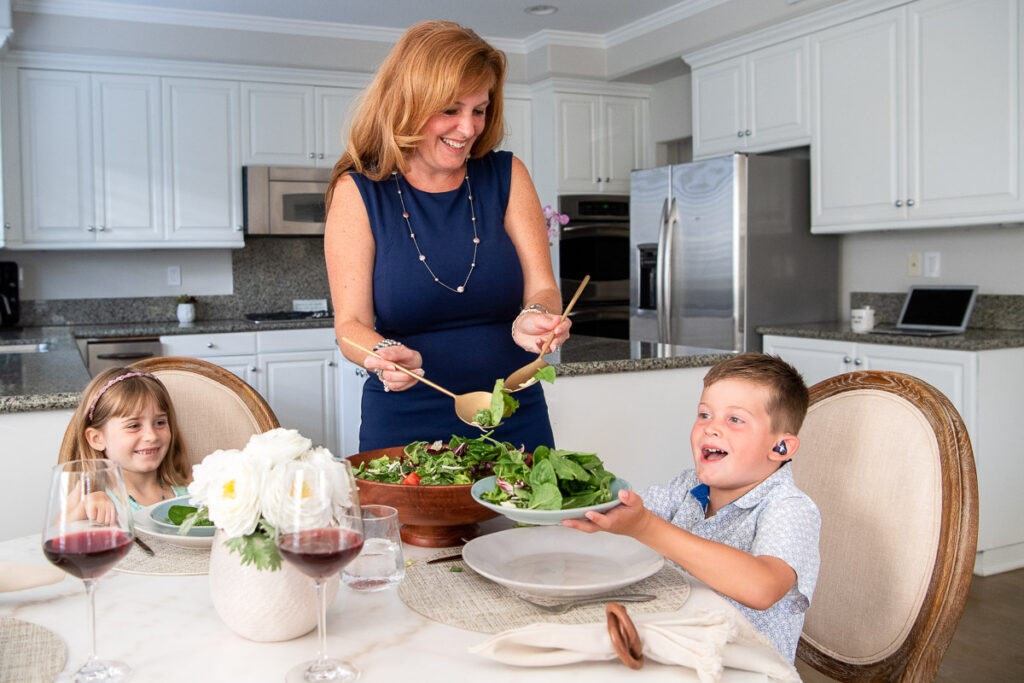 Woman wearing a blue dress, serving a salad to her two kids at the kitchen table