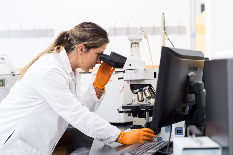 Woman wearing a white lab coat while looking under a microscope