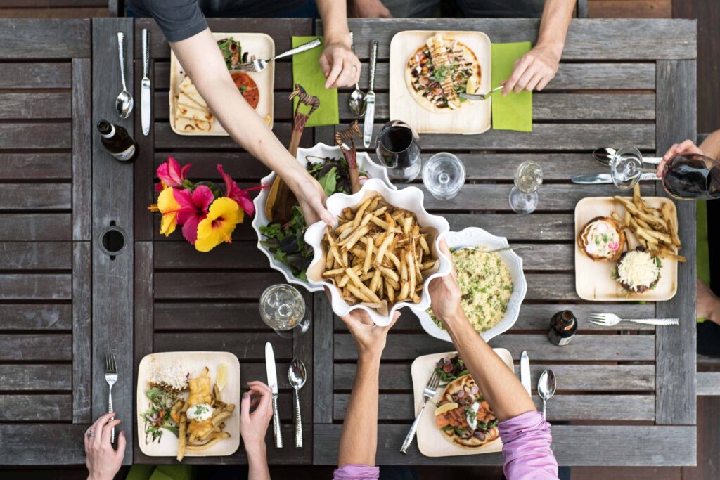 Group of people sitting on a wooden table, sharing and passing food to each other