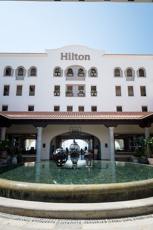 The exterior of a Hilton hotel featuring a decorative fountain with sculptures in front