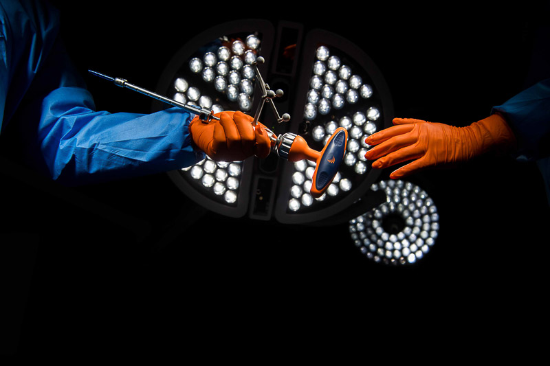 Surgeons passing a medical instrument under bright surgical lights