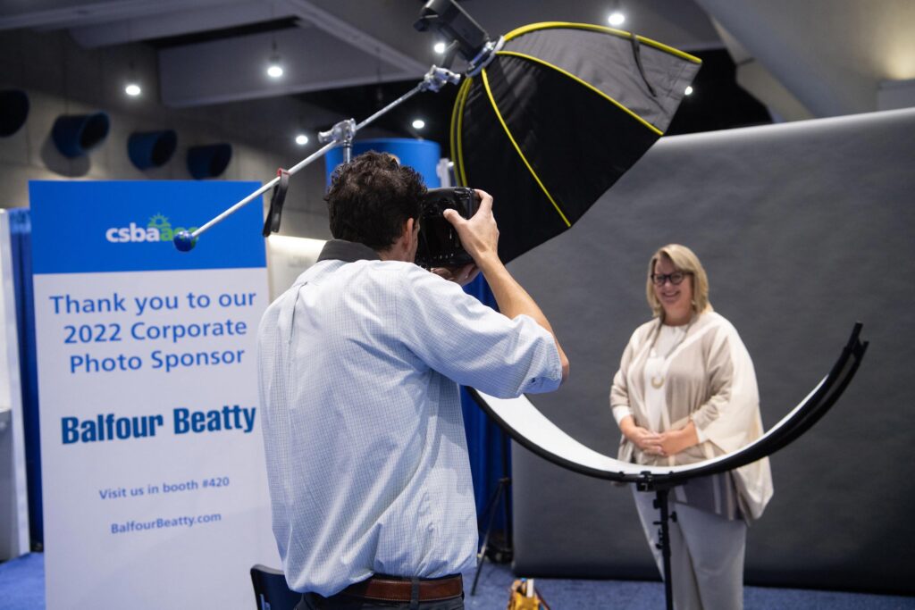 A photographer holding a camera and taking a picture of a woman standing in front of him