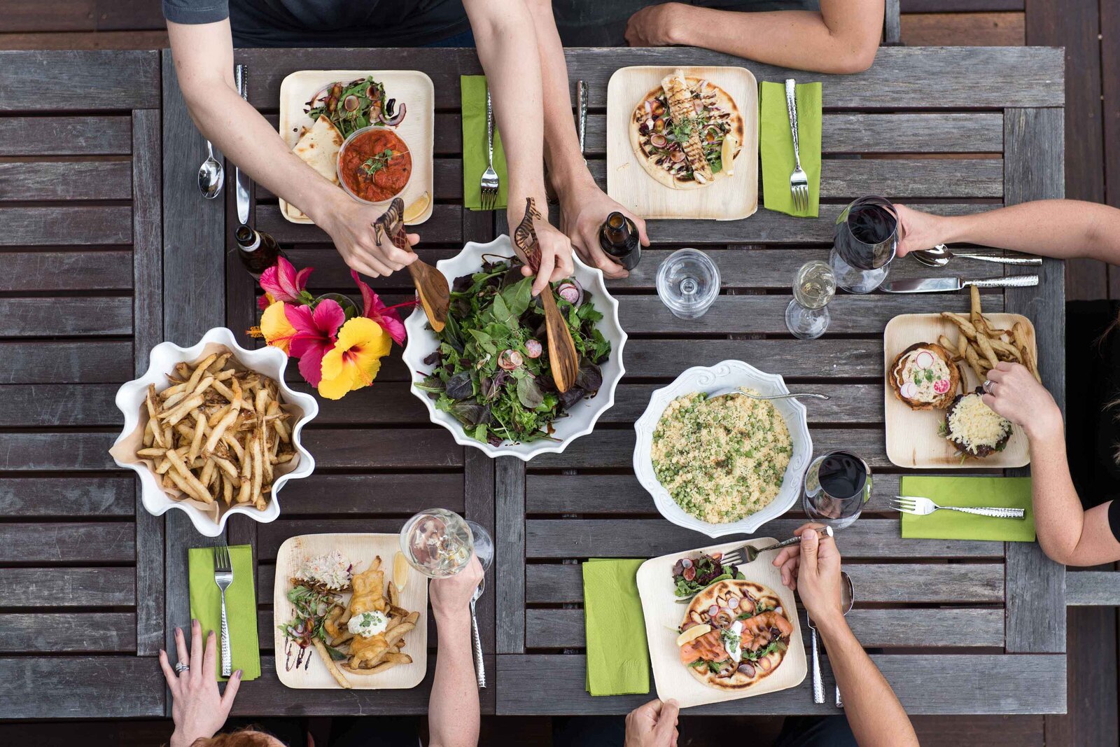 Overhead view of a shared meal on a wooden table with colorful dishes and drinks