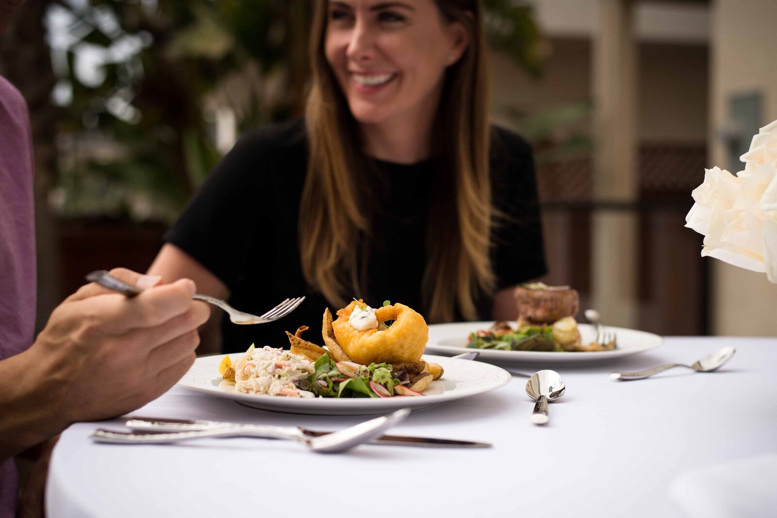 A close-up of plated food with a smiling woman in the background enjoying a meal